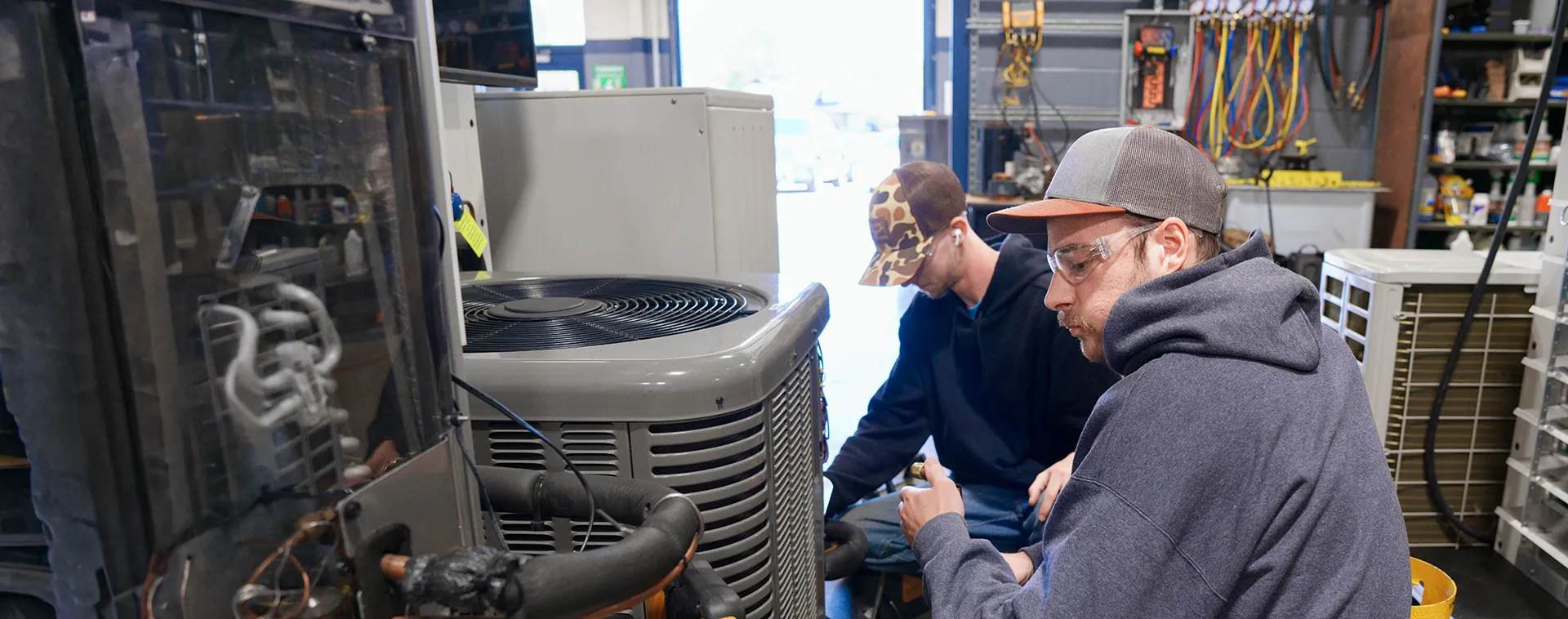 Students work on an HVAC condenser unit in a heating and air conditioning training lab.
