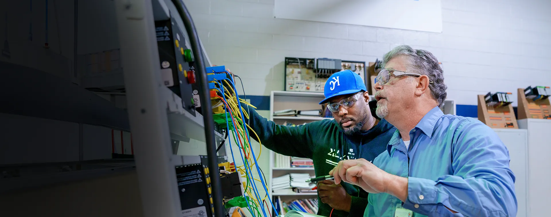 Instructor and student troubleshoot an industrial control panel with wiring in an industrial maintenance training lab.