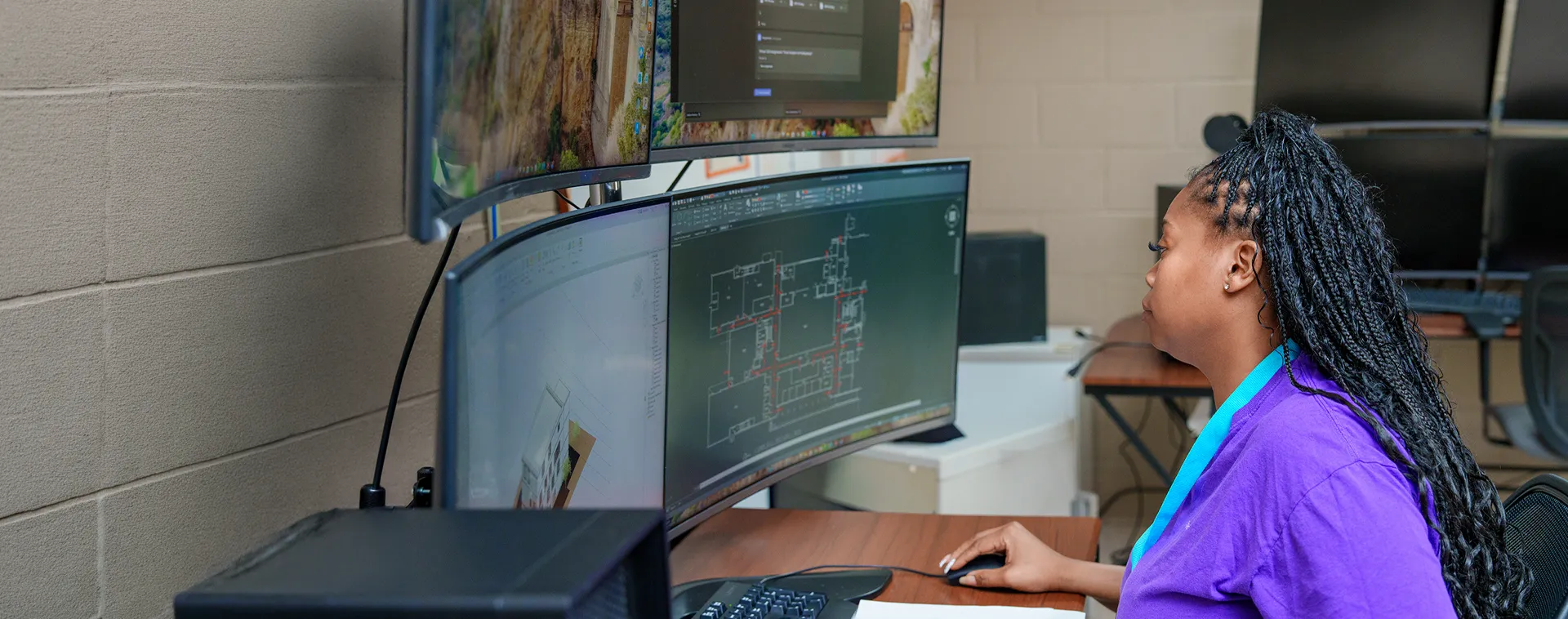 Student works at a multi-monitor workstation displaying architectural drawings and 3D design software.