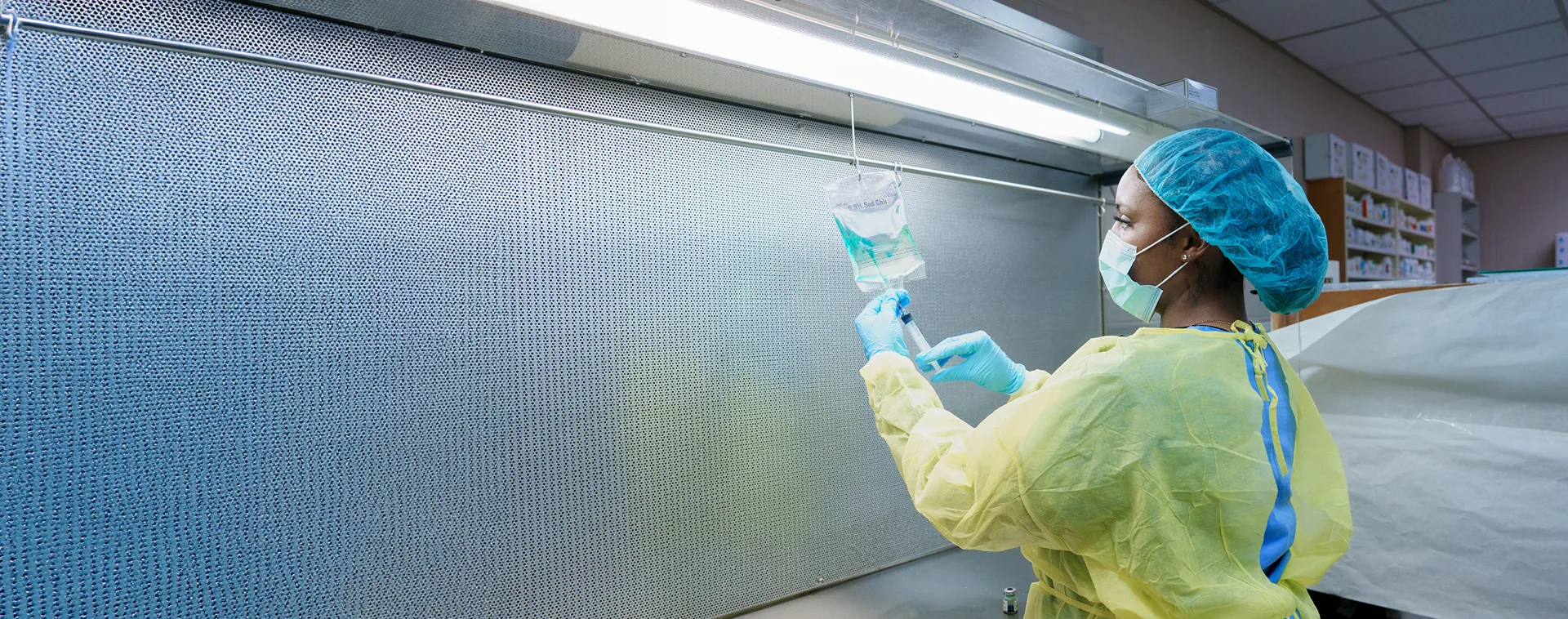 Student in scrubs measures medication from a dispensing device with pharmacy shelves in the background.