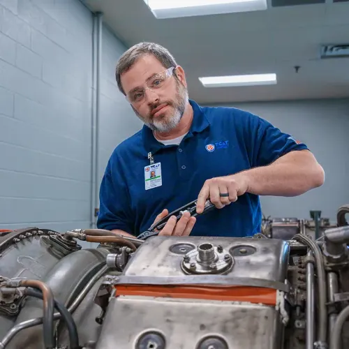 Instructor uses a hand tool on a jet engine component in an aviation maintenance lab.