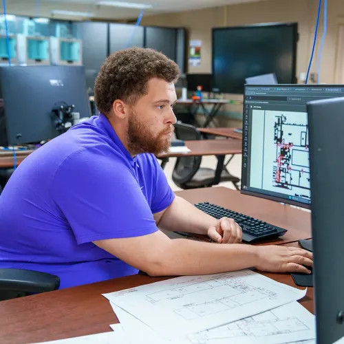 Student views a building floor plan on a computer monitor at a computer-aided design workstation.