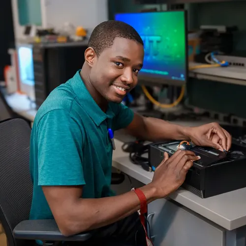 Student seated at a computer workstation looks toward the camera in a computer design lab.