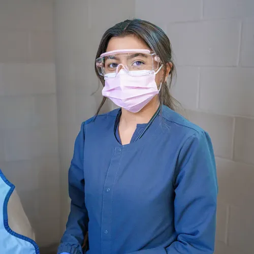 Student wearing protective eyewear and a mask stands in a dental assisting classroom.